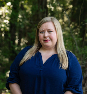 headshot of a person in a blue shirt with forest backdrop headshot of a person in a blue shirt with forest backdrop